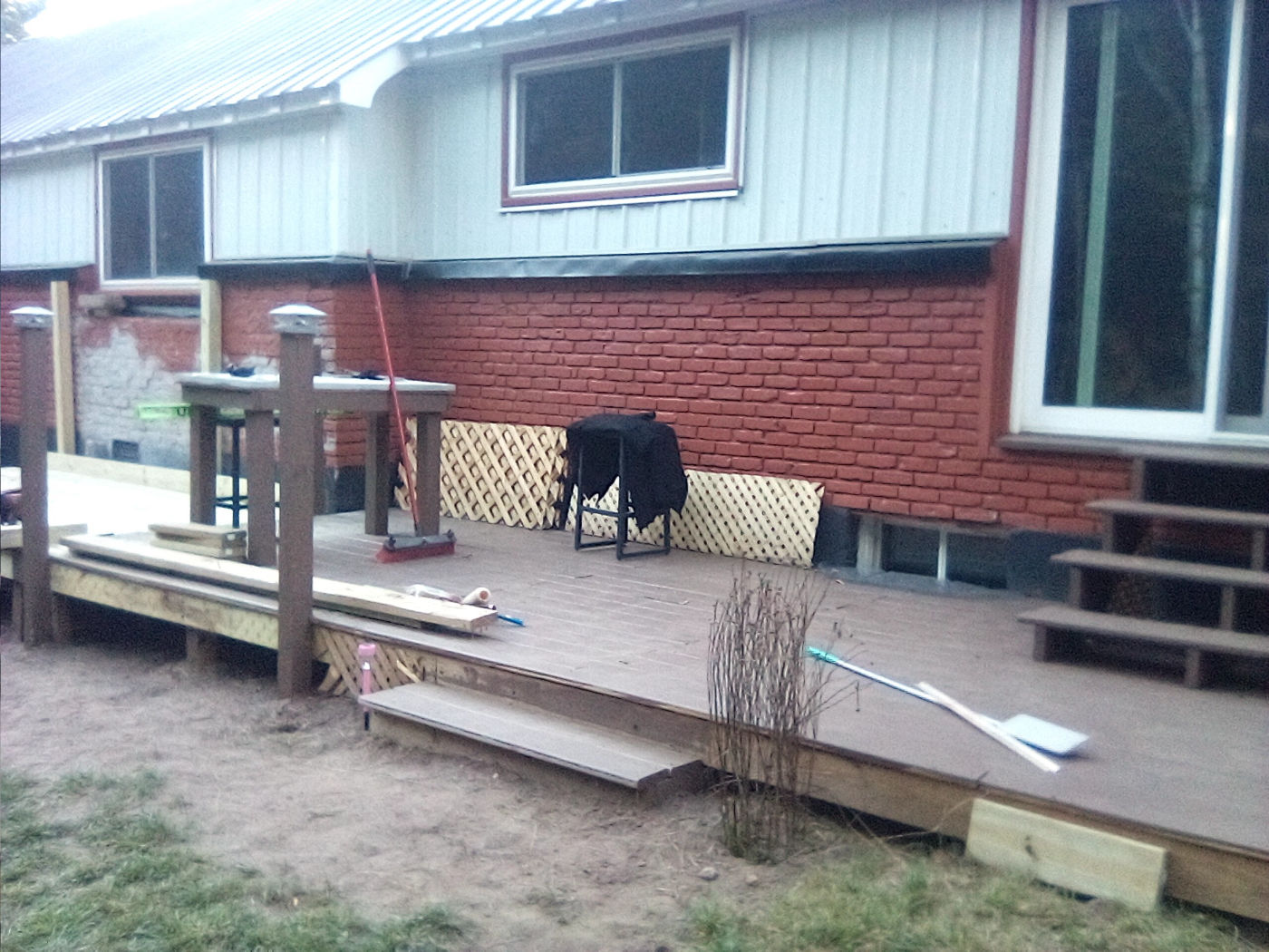Backyard deck with steps, posts, a built-in bar table and lattice skirting, built beside a freshly painted red brick wall